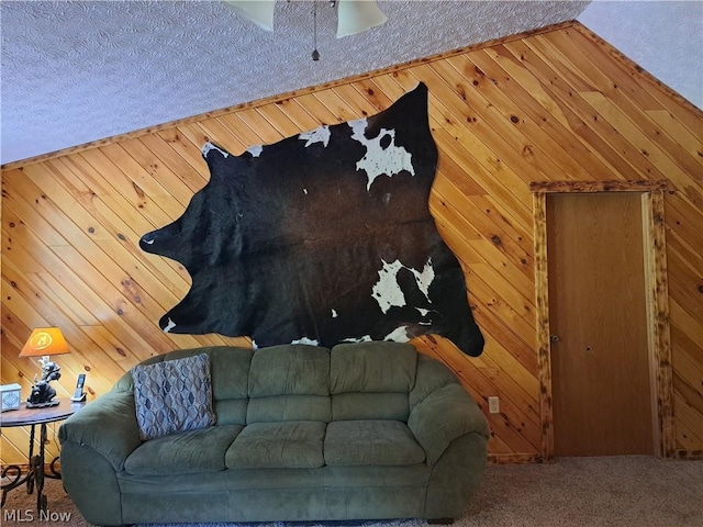 carpeted living room with ceiling fan, wood walls, and a textured ceiling