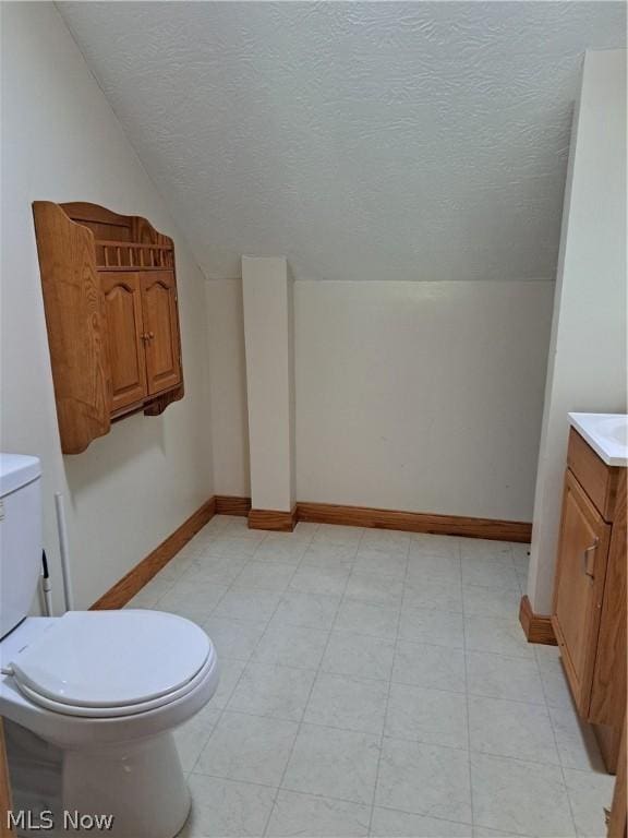 bathroom featuring vanity, toilet, a textured ceiling, and vaulted ceiling