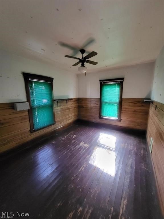 spare room featuring wooden walls, ceiling fan, and dark hardwood / wood-style floors