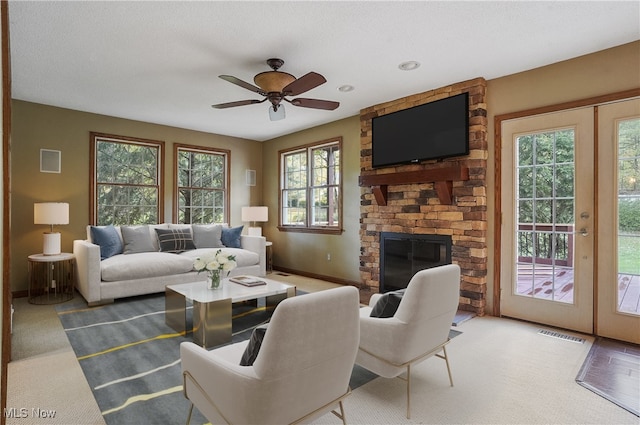 living room featuring ceiling fan, a textured ceiling, a fireplace, and plenty of natural light