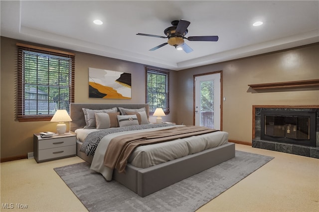 carpeted bedroom with access to exterior, a tile fireplace, multiple windows, and ceiling fan