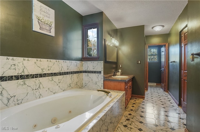 bathroom with a textured ceiling, vanity, and tiled bath