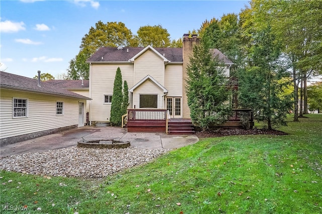 back of property with a wooden deck, a fire pit, a patio, and a lawn