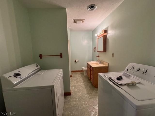 washroom with sink, a textured ceiling, and washing machine and clothes dryer