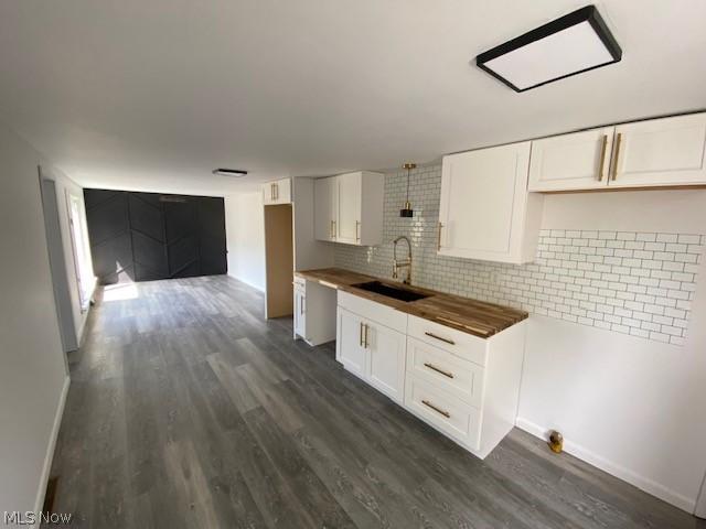 kitchen featuring butcher block countertops, pendant lighting, white cabinetry, and sink