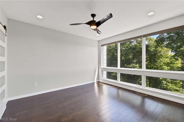 unfurnished room featuring dark hardwood / wood-style floors, a barn door, and ceiling fan