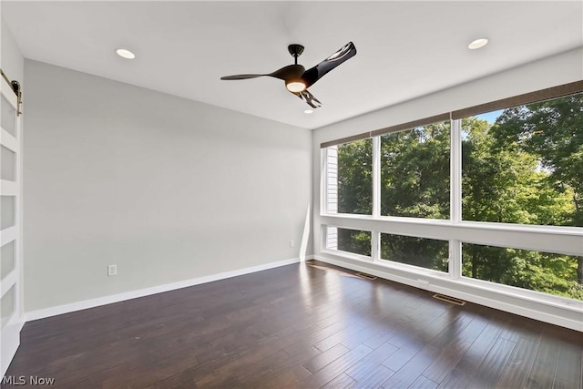 empty room with dark hardwood / wood-style floors, ceiling fan, and a barn door