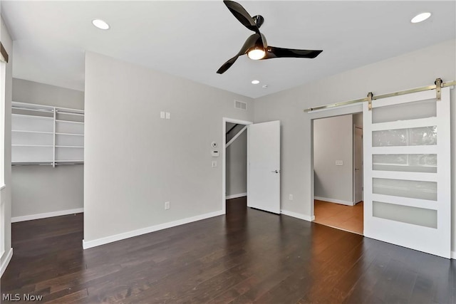 unfurnished bedroom featuring dark wood-type flooring, a spacious closet, a closet, ceiling fan, and a barn door