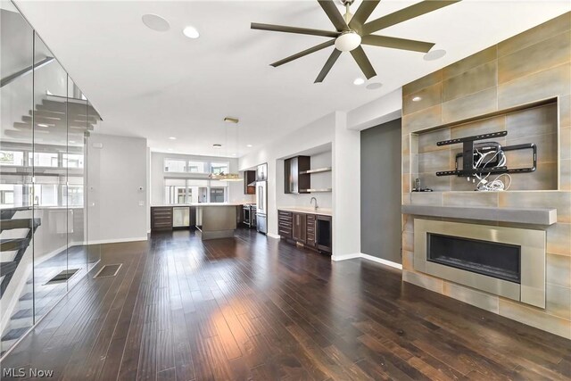 unfurnished living room with dark wood-type flooring, sink, a tiled fireplace, and ceiling fan