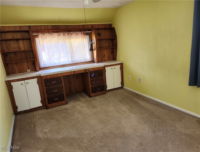 unfurnished office featuring built in desk, light carpet, and lofted ceiling