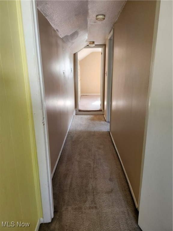 corridor with vaulted ceiling, a textured ceiling, and light colored carpet