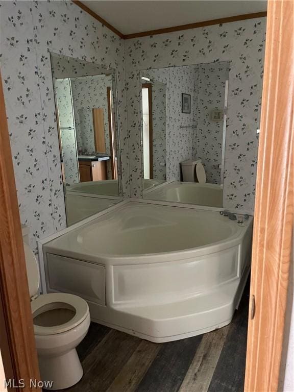 bathroom with hardwood / wood-style floors, a tub to relax in, toilet, and ornamental molding