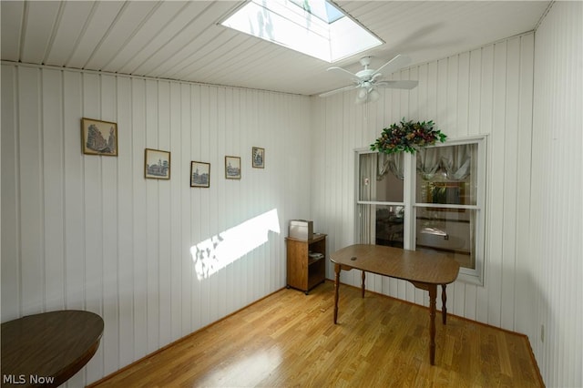 office featuring a skylight, light hardwood / wood-style flooring, ceiling fan, and wooden walls