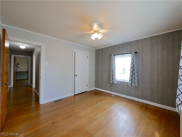 empty room featuring crown molding, ceiling fan, wood-type flooring, and wood walls