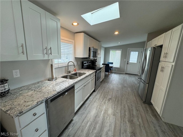 kitchen featuring light stone countertops, appliances with stainless steel finishes, vaulted ceiling with skylight, sink, and white cabinets