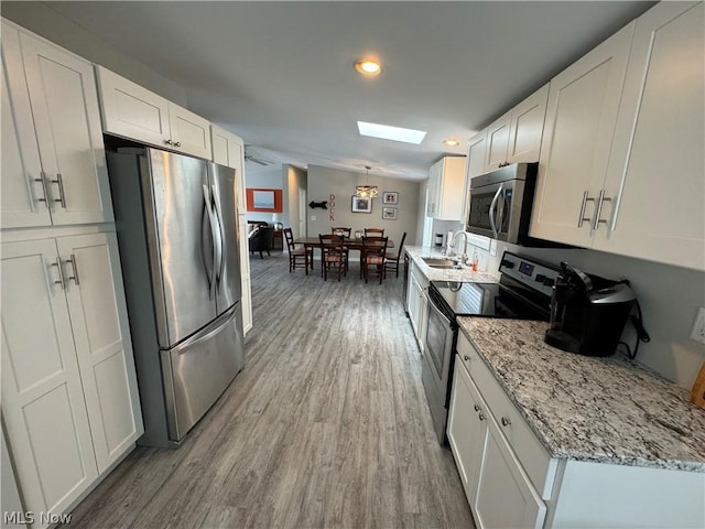 kitchen with a skylight, light stone counters, stainless steel appliances, hardwood / wood-style flooring, and white cabinetry