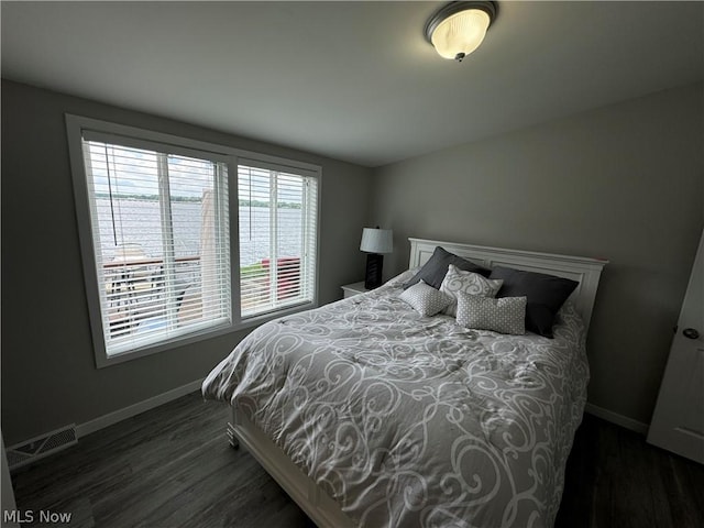 bedroom with dark hardwood / wood-style floors and a water view