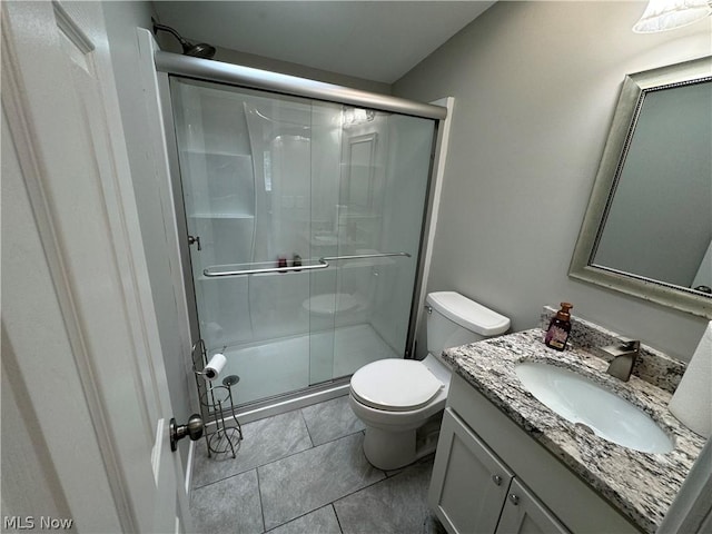 bathroom with tile patterned flooring, vanity, a shower with shower door, and toilet