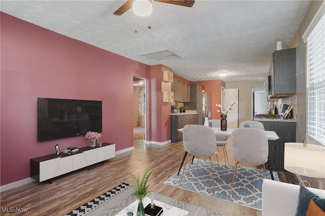 living room featuring ceiling fan, light wood-type flooring, and a textured ceiling