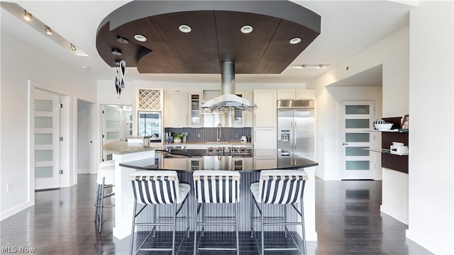 kitchen featuring sink, stainless steel built in refrigerator, backsplash, island range hood, and white cabinets