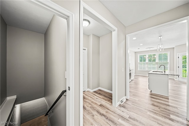 corridor with a notable chandelier, light hardwood / wood-style flooring, and sink