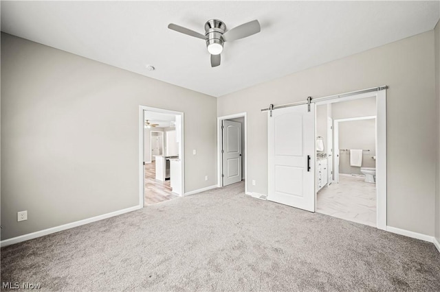 unfurnished bedroom featuring ensuite bathroom, a barn door, carpet flooring, and baseboards