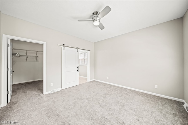 unfurnished bedroom with carpet flooring, a barn door, ceiling fan, a walk in closet, and a closet