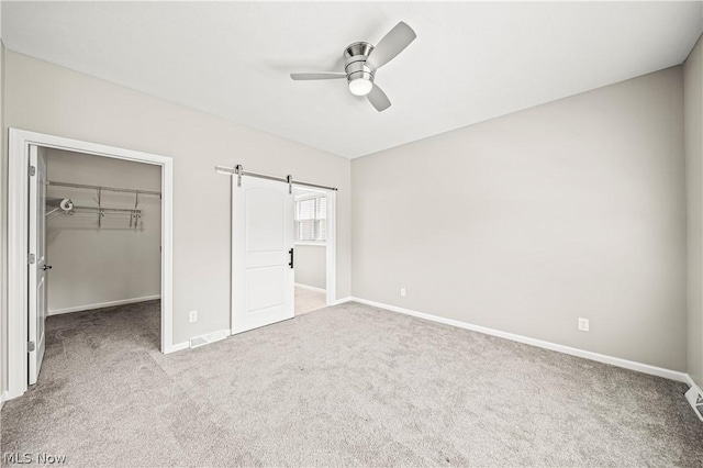 unfurnished bedroom with a barn door, baseboards, a ceiling fan, a spacious closet, and carpet flooring