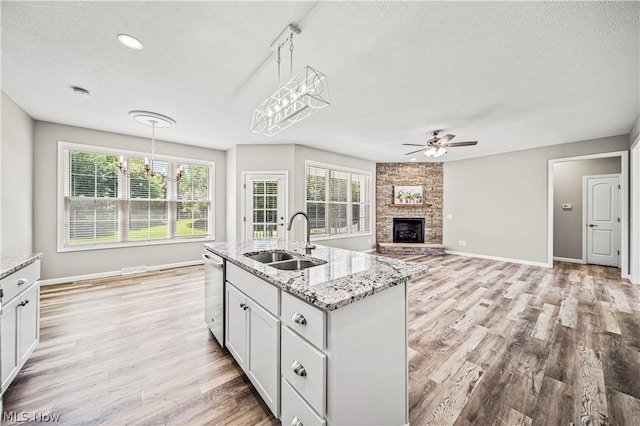 kitchen with light hardwood / wood-style flooring, stainless steel dishwasher, sink, a stone fireplace, and a center island with sink