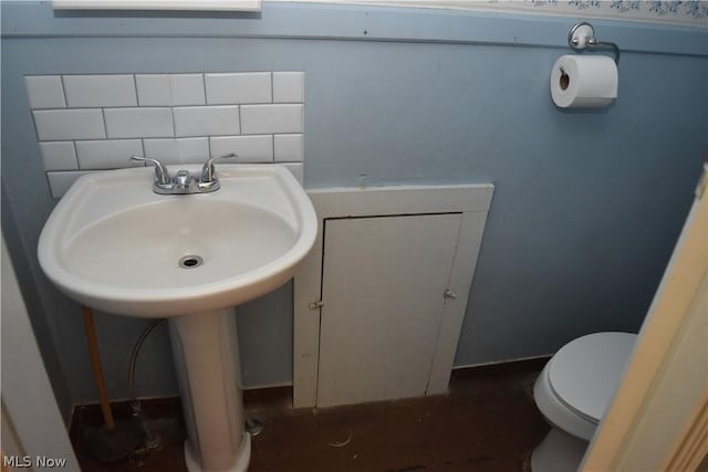 half bathroom with a sink, toilet, and decorative backsplash