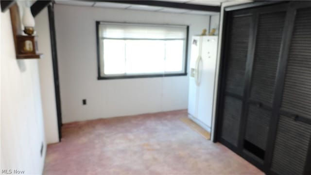 unfurnished bedroom featuring white refrigerator with ice dispenser, light carpet, and a closet