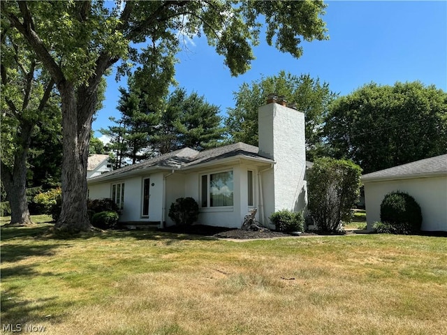 view of front of house featuring stucco siding, a chimney, and a front yard