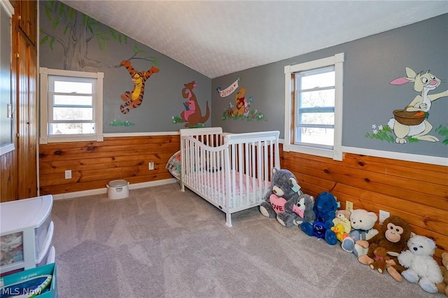 bedroom featuring wood walls, a nursery area, carpet, a textured ceiling, and vaulted ceiling