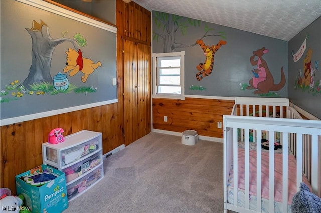 carpeted bedroom with a textured ceiling, wooden walls, and a crib