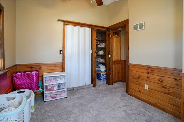 bedroom featuring ceiling fan, light carpet, and wood walls