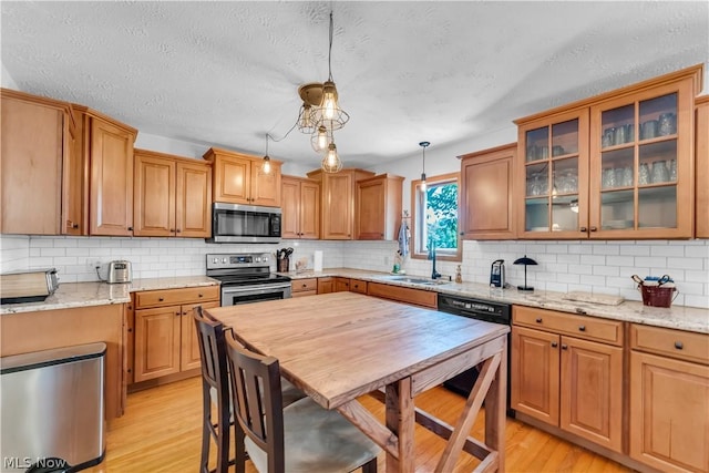 kitchen featuring appliances with stainless steel finishes, light hardwood / wood-style flooring, light stone countertops, pendant lighting, and sink