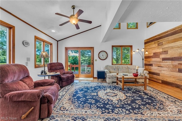 living room featuring ornamental molding, lofted ceiling, wooden walls, and ceiling fan