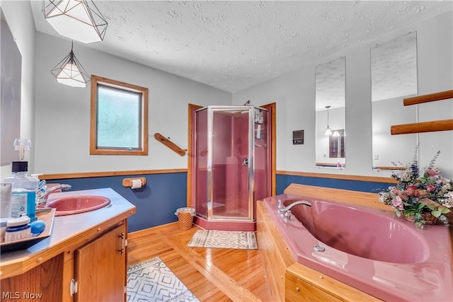 bathroom with a textured ceiling, hardwood / wood-style flooring, plus walk in shower, and vanity