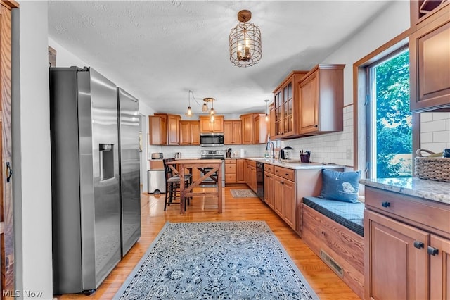 kitchen featuring hanging light fixtures, light stone countertops, stainless steel appliances, and light hardwood / wood-style floors