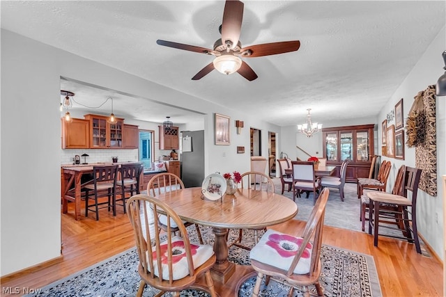 dining space with a textured ceiling, ceiling fan with notable chandelier, and light hardwood / wood-style flooring