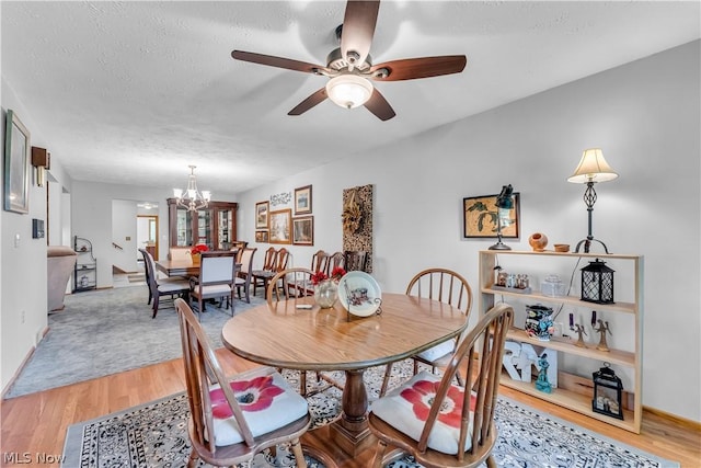 dining area featuring ceiling fan with notable chandelier, wood-type flooring, and a textured ceiling