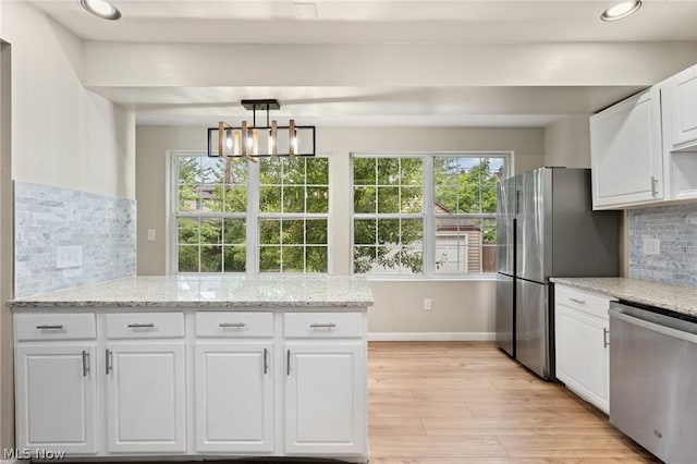 kitchen featuring stainless steel appliances, white cabinets, light stone counters, backsplash, and a chandelier