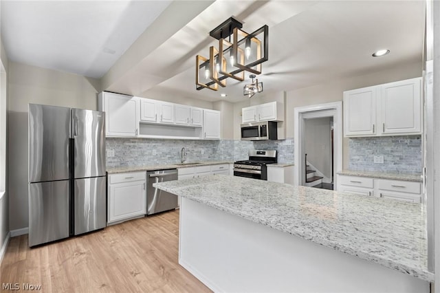 kitchen featuring white cabinetry, appliances with stainless steel finishes, sink, light hardwood / wood-style flooring, and decorative light fixtures