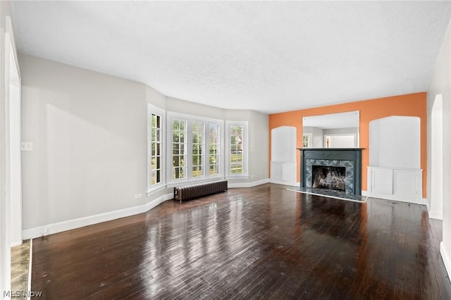 unfurnished living room featuring a high end fireplace, radiator heating unit, and hardwood / wood-style floors