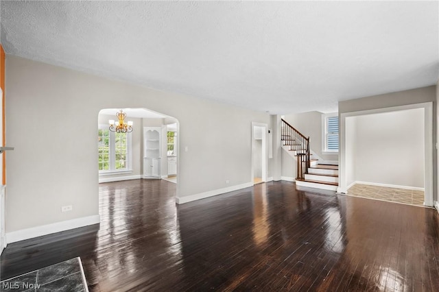 unfurnished living room with an inviting chandelier, a textured ceiling, and dark hardwood / wood-style flooring