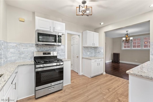 kitchen with appliances with stainless steel finishes, pendant lighting, white cabinets, and radiator heating unit