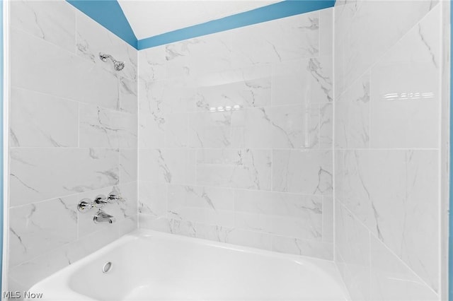 bathroom featuring vaulted ceiling and tiled shower / bath