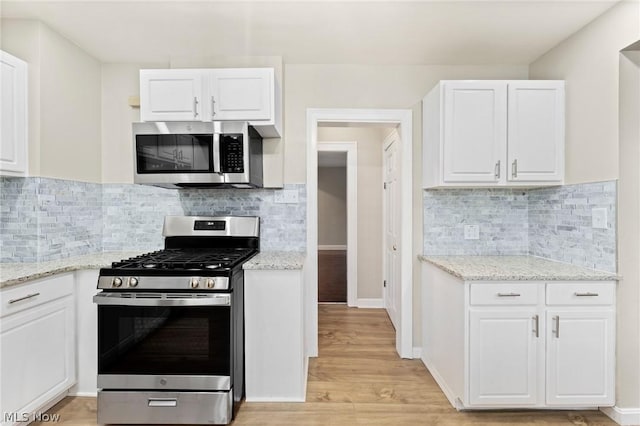 kitchen featuring stainless steel appliances, white cabinetry, backsplash, and light stone counters