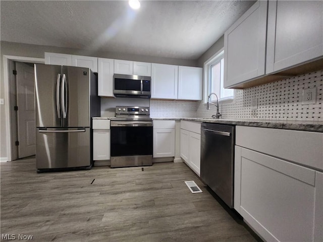 kitchen with sink, light hardwood / wood-style flooring, decorative backsplash, white cabinets, and appliances with stainless steel finishes