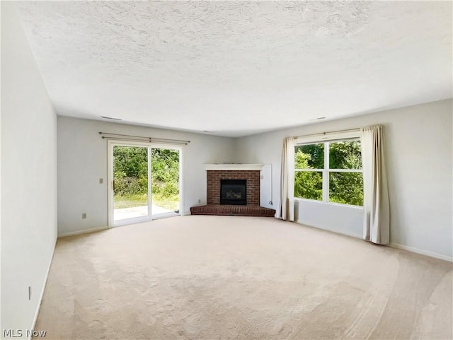 unfurnished living room with a textured ceiling, light colored carpet, and a brick fireplace